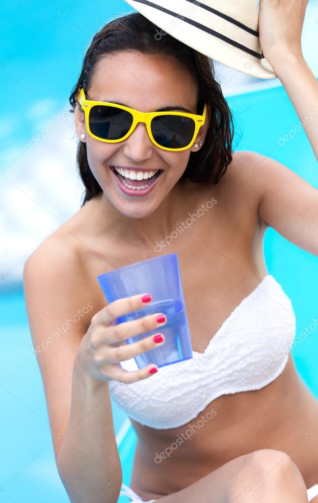 Beautiful girl drinking water at the swimming pool.