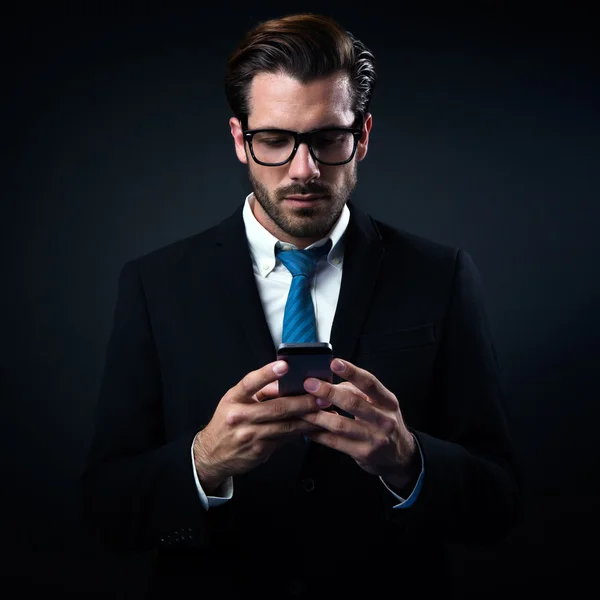 Knappe stijlvolle man in elegant zwart pak met behulp van mobiele telefoon. — Stockfoto