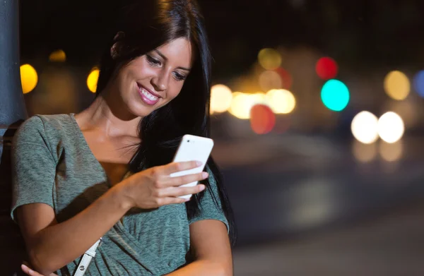Mulher bonita usar seu telefone na cidade à noite . — Fotografia de Stock