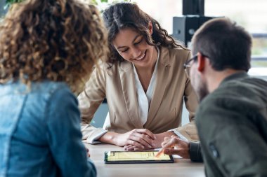 Güzel bir emlakçının elektronik tablette ev planlarını gösterirken olgun bir adamla gayrimenkul satın alma hakkında konuşurken çekilmesi.