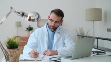 Tıbbi konsültasyonda bilgisayarla çalışan olgun, konsantre ve çekici bir erkek doktorun videosu..