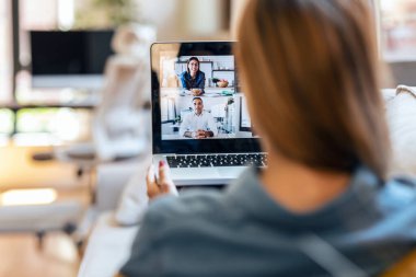 Yetişkin bir iş kadınının video konferansında çeşitli meslektaşlarıyla evdeki kanepede dizüstü bilgisayarla yaptığı brifingde konuşması..