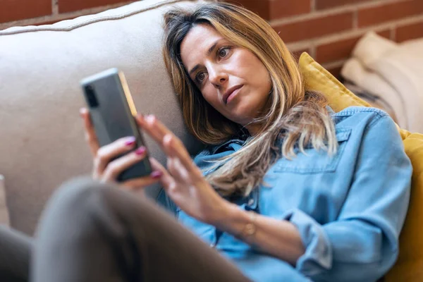 Ditembak Wanita Dewasa Menggunakan Ponsel Sambil Bersantai Duduk Sofa Rumah — Stok Foto