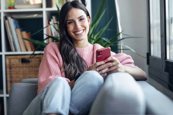 Snímek Krásné Usměvavé Ženy Pomocí Mobilního Telefonu Sedí Gauči Doma — Stock fotografie