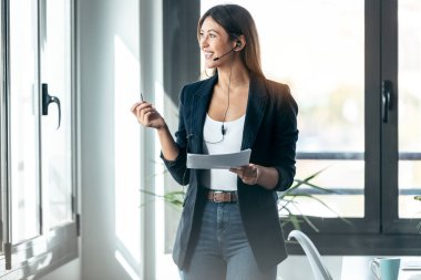 Modern bir ofisteki bazı belgelere bakarken zarif bir iş kadınının kulaklıkla konuşması..