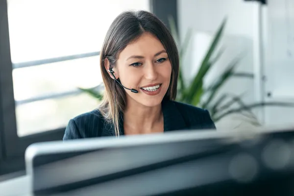 매력적 사업가가 컴퓨터로 비디오 통화를 하면서 스타트업 사무실에 이어폰으로 통화하는 — 스톡 사진