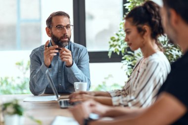 Ofiste yeni projelerinden bahsederken dizüstü bilgisayarlarla çalışan çok yönlü iş adamlarının fotoğrafları..