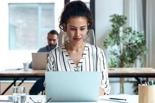 現代のスタートアップオフィスでデスクに座っている間にコンピュータで働く魅力的な若いビジネス女性のショット — ストック写真