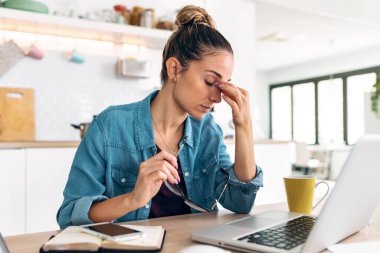 Stresli bir iş kadınının evde dizüstü bilgisayarla çalışırken endişeli, yorgun ve bunalmış görünmesi.. 