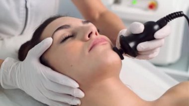 Kozmetik bilimci videosu, bu prosedürü güzellik merkezindeki genç ve güzel bir kadının yüz derisinin ultrasonik olarak temizlenmesi haline getiriyor..