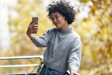 Evdeki balkonda dikilirken akıllı telefonuyla fotoğraf çeken güzel bir kadın..