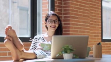 Mutlu bir kadının yemek çubuklarıyla erişte yerken evdeki oturma odasında dizüstü bilgisayarla yaptığı görüntüler..