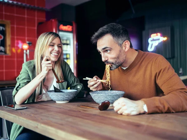 アジア料理店で楽しみながら箸でラーメンを食べる幸せなカップルのショット — ストック写真