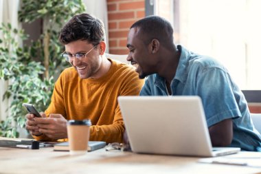 Modern bir ofiste cep telefonunda komik şeyler ararken iki grafik tasarımcısının fotoğraf çekimi..