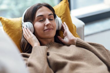Evdeki kanepede uzanmış akıllı telefon kullanırken güzel bir kadının kulaklıkla müzik dinlemesi..