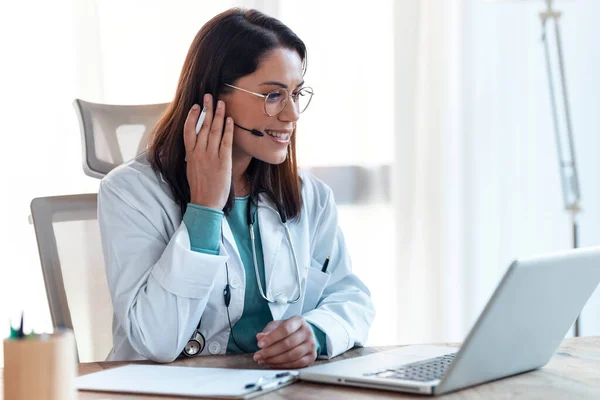 診察中のノートパソコンやイヤホンを使ったビデオ通話で患者さんへの医療説明をしながら話す女性医師のショット — ストック写真