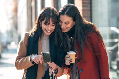İki güzel turist arkadaşının sokakta akıllı bir telefondan internet rehberine danışması..