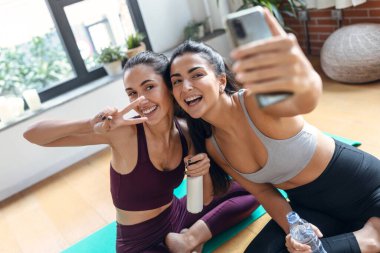 Evdeki spor salonundaki çevrimiçi derslerden sonra akıllı telefonuyla selfie çeken iki genç kadının fotoğrafı..