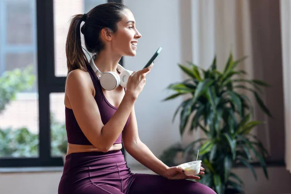 Spor Yapan Genç Bir Kadının Yoğurt Yerken Akıllı Telefonu Evde — Stok fotoğraf