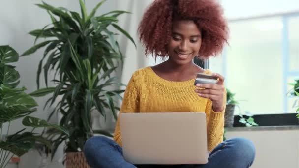 自宅のリビングルームでパフに座っている間 彼女のクレジットカードでオンラインで何かを支払うリラックスした女性のビデオ — ストック動画