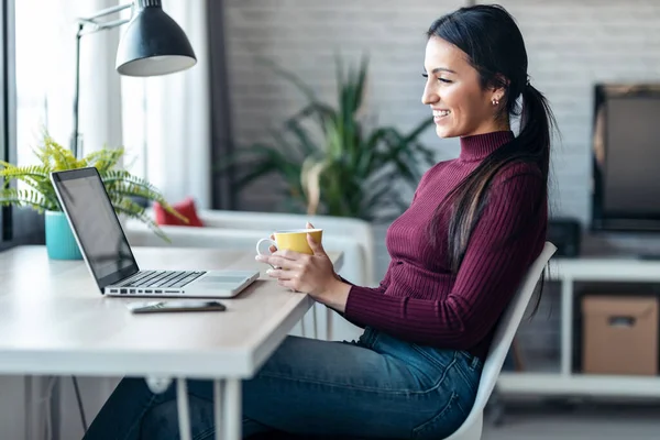 自宅のオフィスでコーヒーを飲みながらコンピュータを操作する濃縮若いビジネス女性のショット — ストック写真