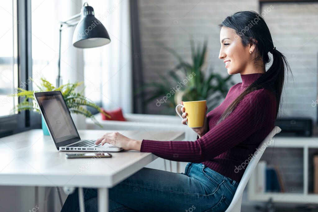Shot of concentrated young business woman working with computer while drinking coffee in the office at home.