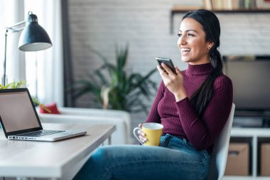 İş kadınının evde çalışırken ve kahve içerken cep telefonuyla mesaj göndermesi..