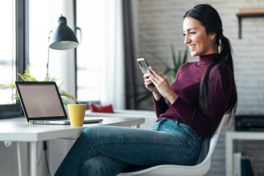 İş kadınının evde çalışırken ve kahve içerken cep telefonuyla mesaj göndermesi..