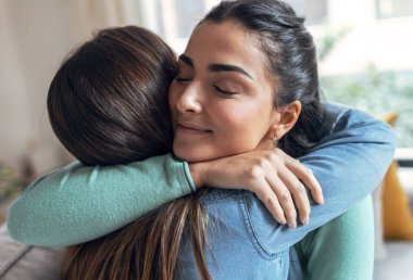 Evdeki oturma odasında otururken birbirine sarılan iki güzel kadının portresi..