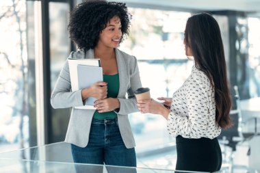 Modern bir girişimde konuşurken ve yürürken dijital tabletle çalışan iki çekici genç iş kadınının fotoğrafı.. 