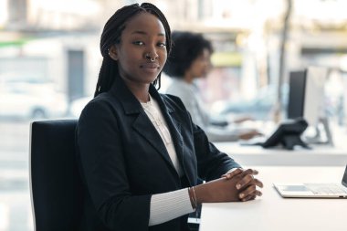 Modern bir girişimde kameraya bakarken dizüstü bilgisayarla çalışan zarif bir iş kadını fotoğrafı..