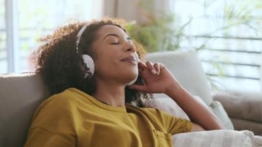 Güzel, olgun bir kadının akıllı telefonuyla müzik dinleyip evdeki koltukta dinlendiği bir video..