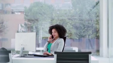 Ofiste bilgisayarla çalışırken cep telefonuyla konuşan zeki bir iş kadınının videosu..
