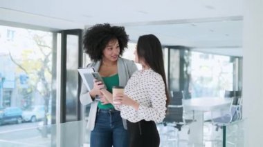 Modern bir girişimde konuşurken ve yürürken dijital tabletle çalışan iki çekici genç iş kadınının videosu. 