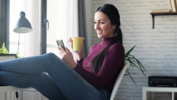 自宅でコーヒーを飲みながら仕事をしながら携帯電話でメッセージを送る美容ビジネス女性のビデオ — ストック動画