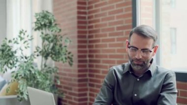 Modern bir ofiste bilgisayarla çalışırken akıllı telefonlu mesajlar gönderen yakışıklı girişimci videosu.