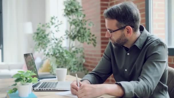 Ofiste Defterine Notlar Yazarken Bilgisayarla Çalışan Yakışıklı Bir Adamının Videosu — Stok video