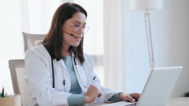 在会诊过程中 女医生通过带笔记本电脑和耳机的视频电话向病人解释治疗情况时谈话的视频 — 图库视频影像
