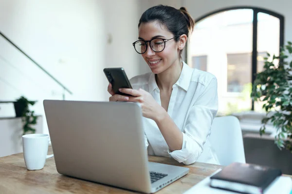 Ofiste Bilgisayarla Çalışırken Gülümseyen Kadınının Cep Telefonunu Kullanması — Stok fotoğraf