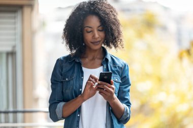 Evdeki balkonda mesaj gönderirken akıllı telefonunu kullanan neşeli bir kadının fotoğrafı..