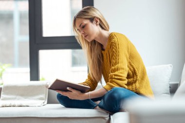 Evdeki kanepede oturmuş kitap okuyan güzel bir genç kadın..