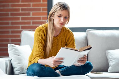 Evdeki kanepede oturmuş kitap okuyan güzel bir genç kadın..