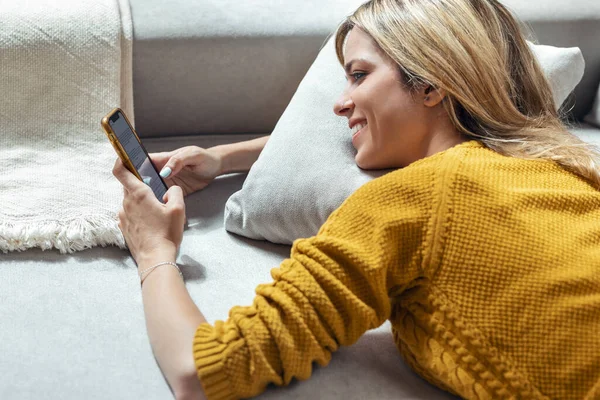 自宅のソファに横たわっている間 携帯電話を使用してかなり笑顔の女性のショット — ストック写真