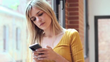 Evde pencerenin yanında duran genç bir kadının cep telefonunu kullanışının videosu..