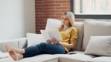 Evdeki kanepede oturmuş kitap okuyan güzel bir genç kadının videosu..