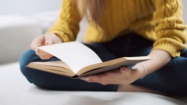 Evdeki kanepede oturmuş kitap okuyan güzel bir genç kadının yakın çekim videosu..