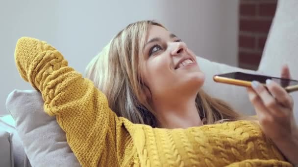 一个漂亮的微笑的女人躺在沙发上用手机拍摄的视频 — 图库视频影像