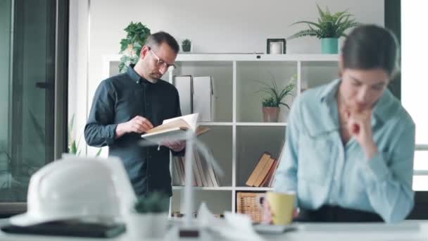 Video Chytrého Architekta Jak Čte Knihu Zatímco Jeho Kolega Pracuje — Stock video