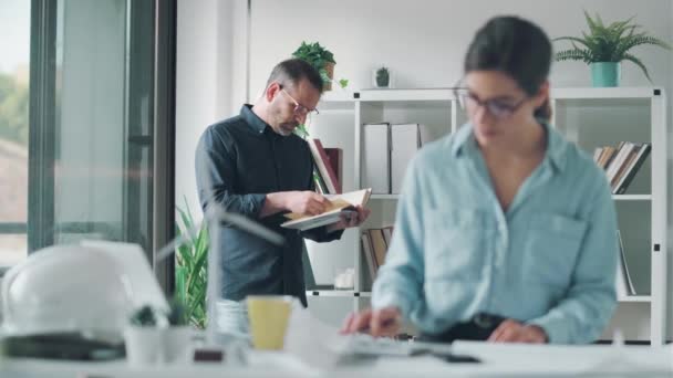 Vídeo Arquiteto Masculino Inteligente Lendo Livro Enquanto Seu Colega Trabalha — Vídeo de Stock