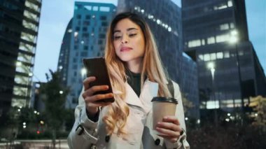 Zarif bir kadının elinde bir fincan kahve tutarken sokakta duran akıllı telefonlu mesajlar gönderdiği bir video..